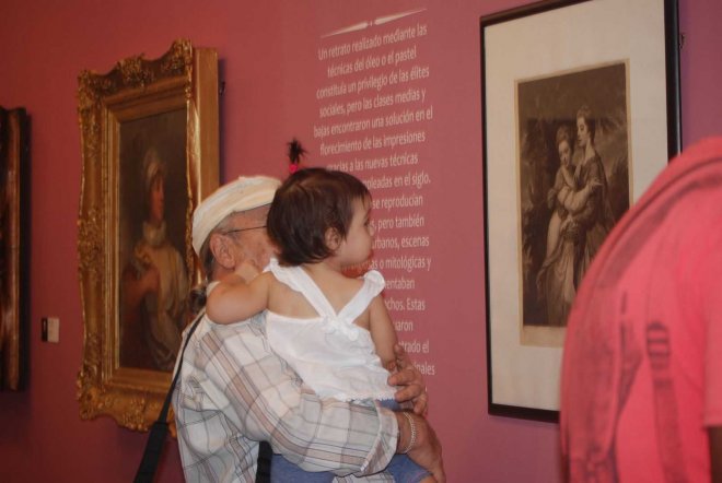 El crítico de arte, Antonio Fernández Seoane, sostiene a la visitante más joven de la muestra